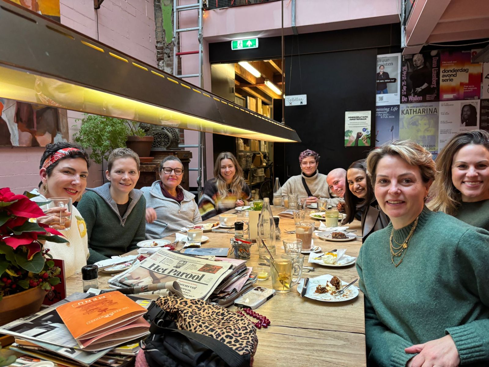 Members of Cancer Support Netherlands smiling around a long café table with coffee and cake