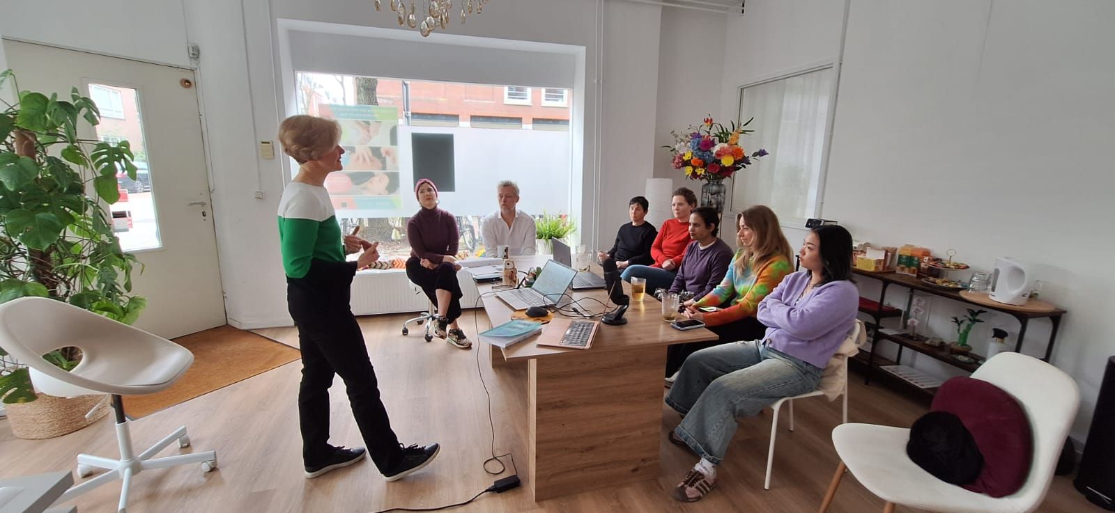 A speaker giving a talk to a small group seated around a table in a bright room