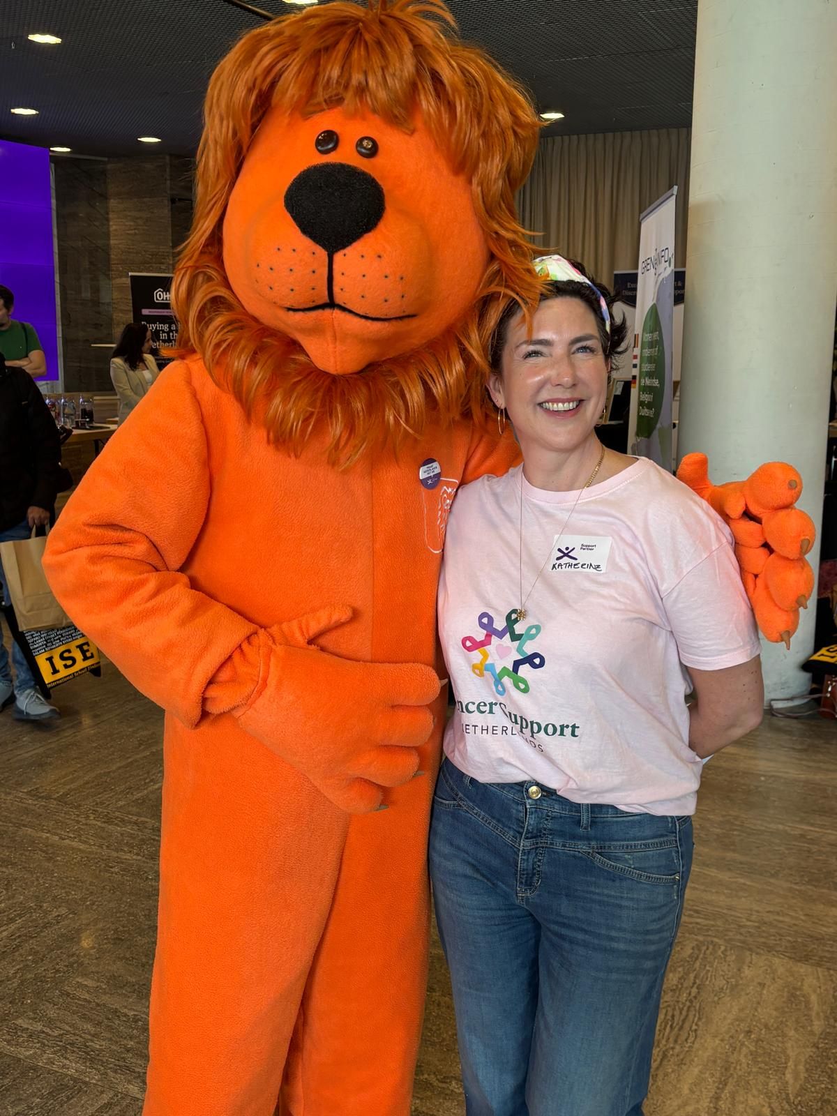 Katherine in a pink CSN T-shirt next to an orange lion mascot at an expo
