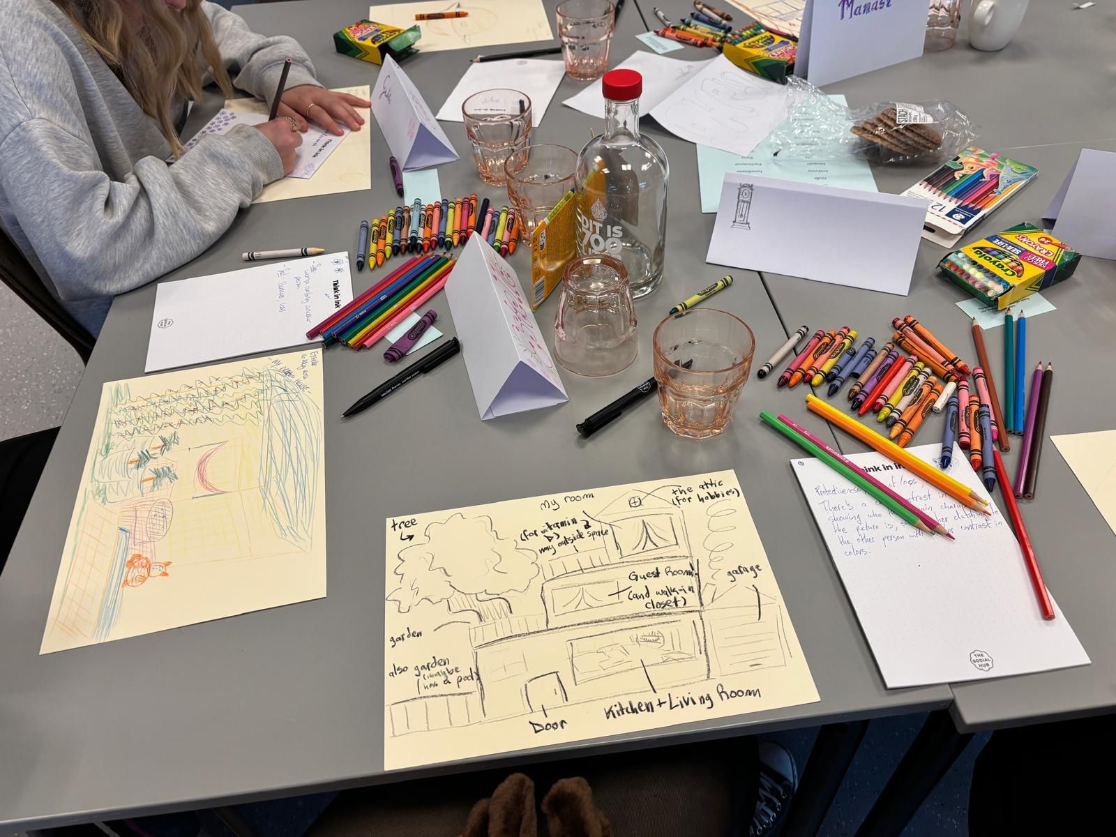 A table covered in crayons, coloured pencils and drawings of houses made during a CSN creative workshop